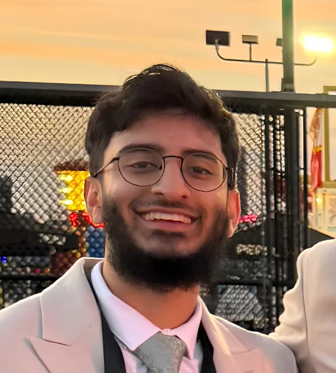 Portrait of Ibrahim Ayub Desai, smiling, wearing glasses and a light suit